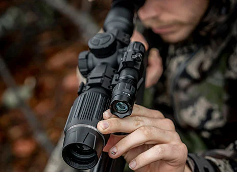 A hunter places his hand on his night vision scope, steadying it as he takes aim.